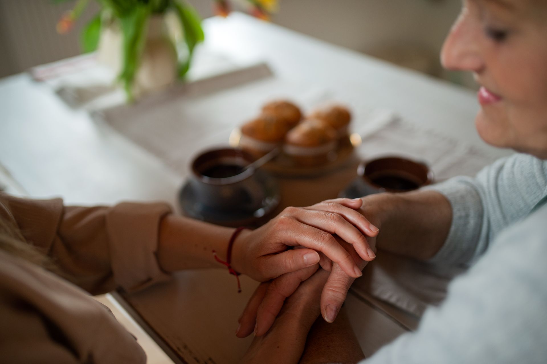 Two people holding hands over a table with coffee and muffins in a home setting.
