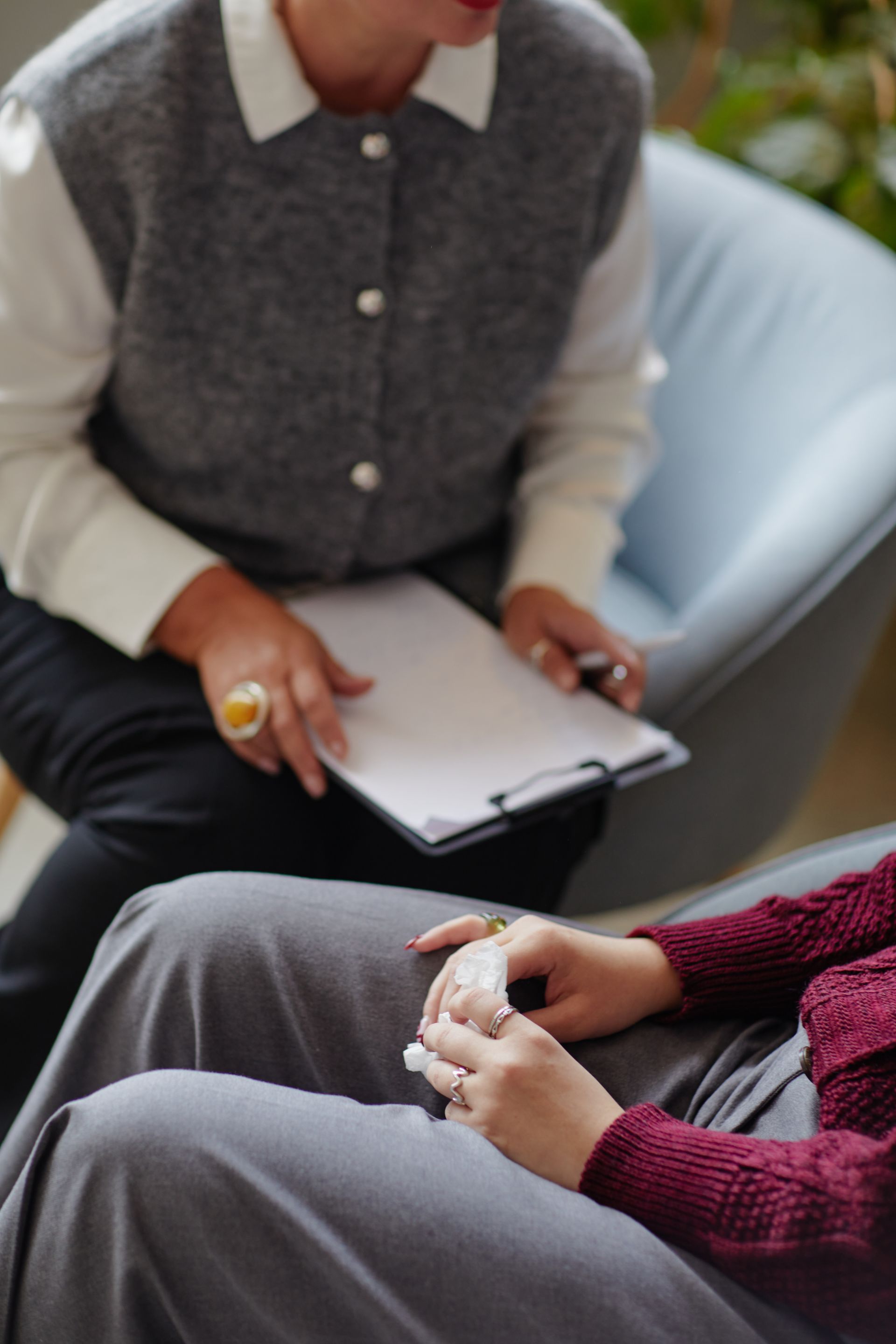 Two people seated in chairs, one holding a clipboard and the other resting their hands on their lap.