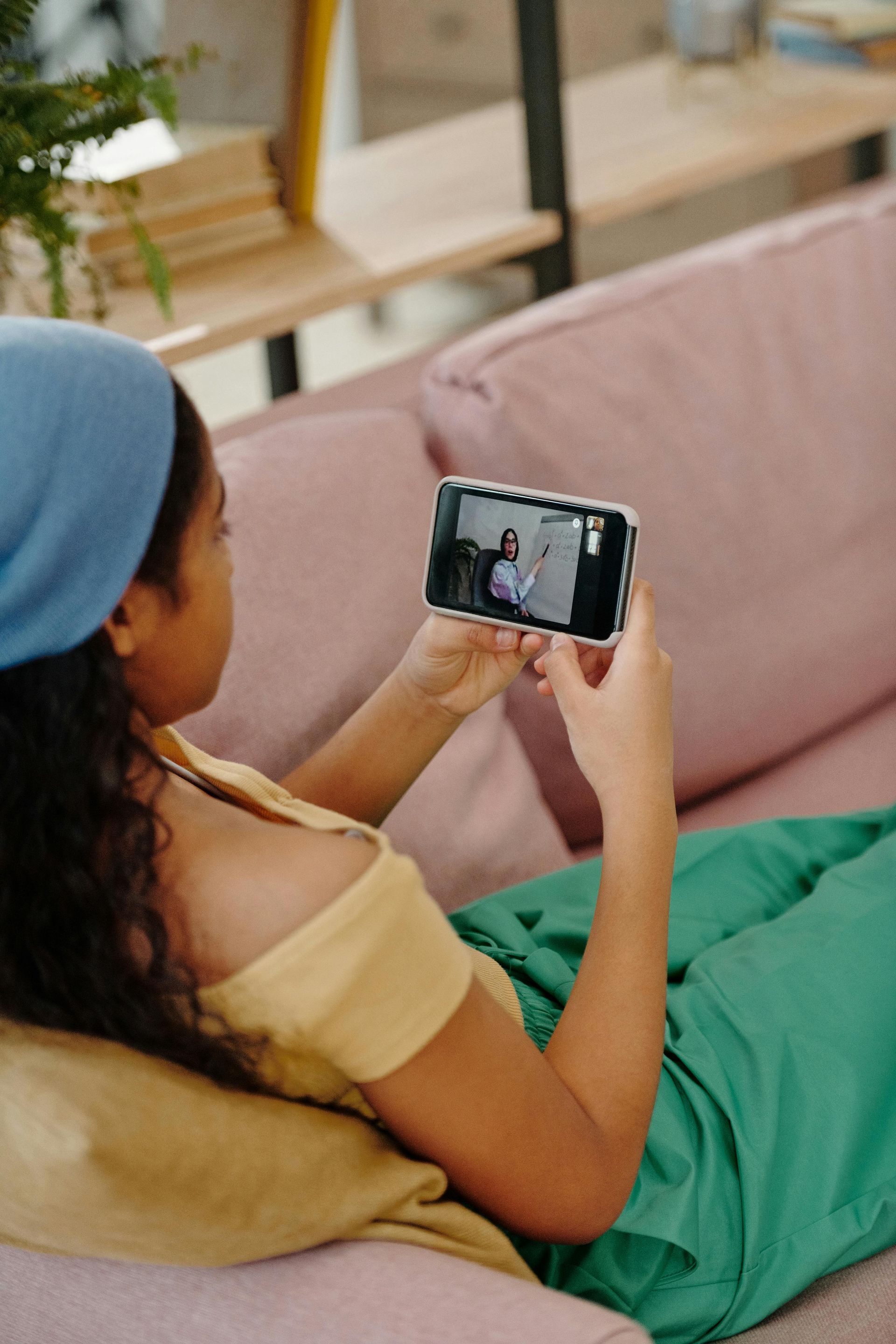 Person on a couch watching a video on a smartphone while covered with a green blanket