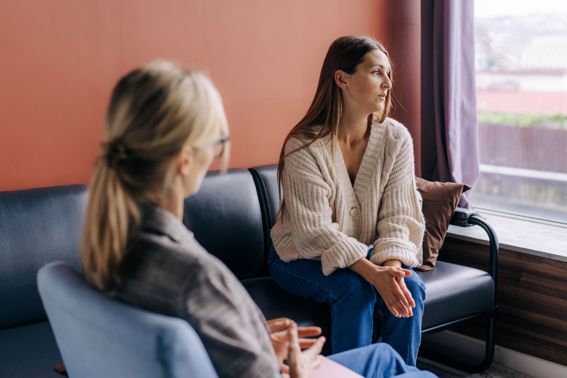 Two people seated in a room, with one person listening to the other in a professional or therapeutic setting.