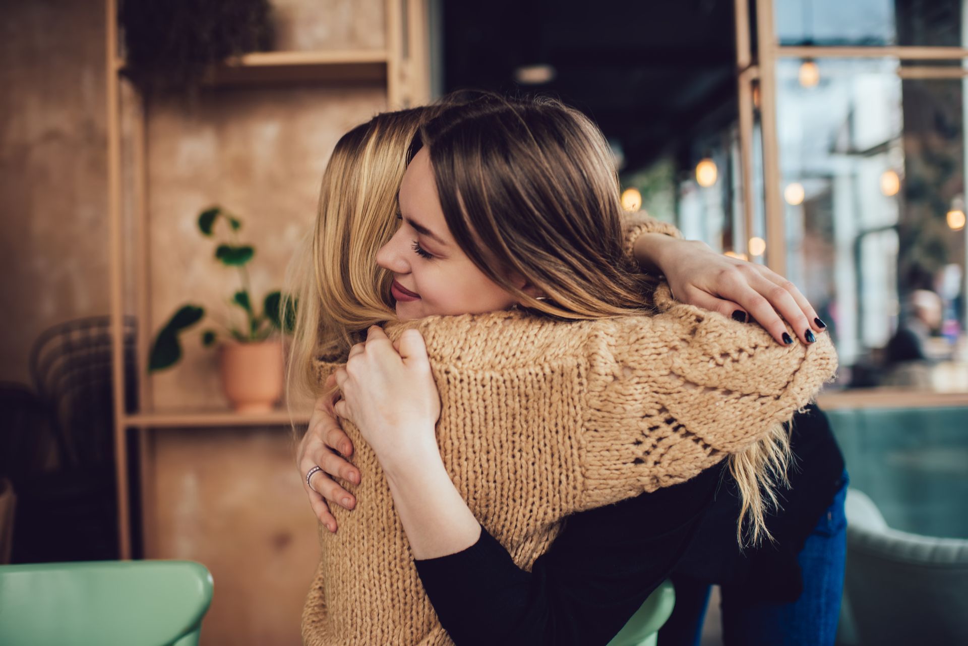 Two people share a warm embrace in a softly lit, modern cafe setting.