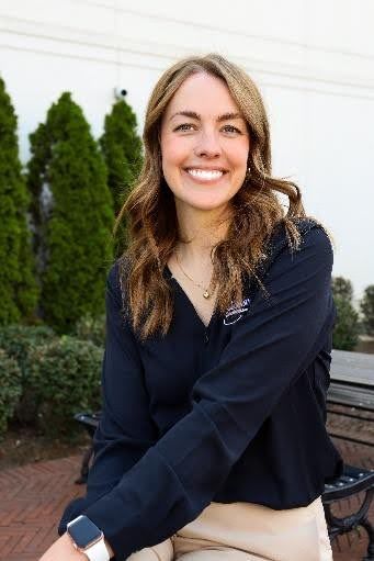 Woman in blue shirt smiles in front of a backdrop with a logo.