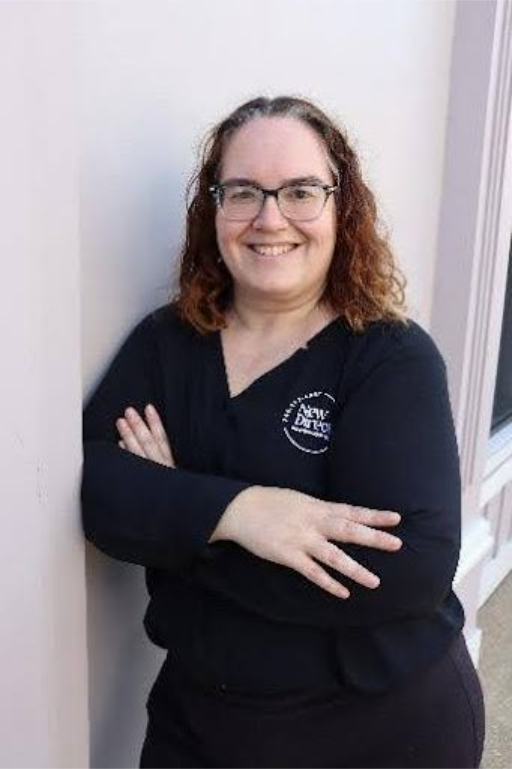 Woman in blue shirt smiles in front of a backdrop with a logo.