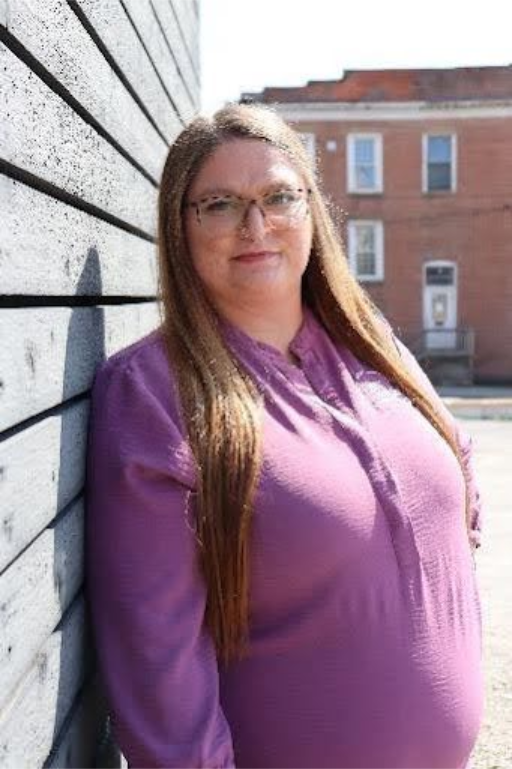 Woman in blue shirt smiles in front of a backdrop with a logo.