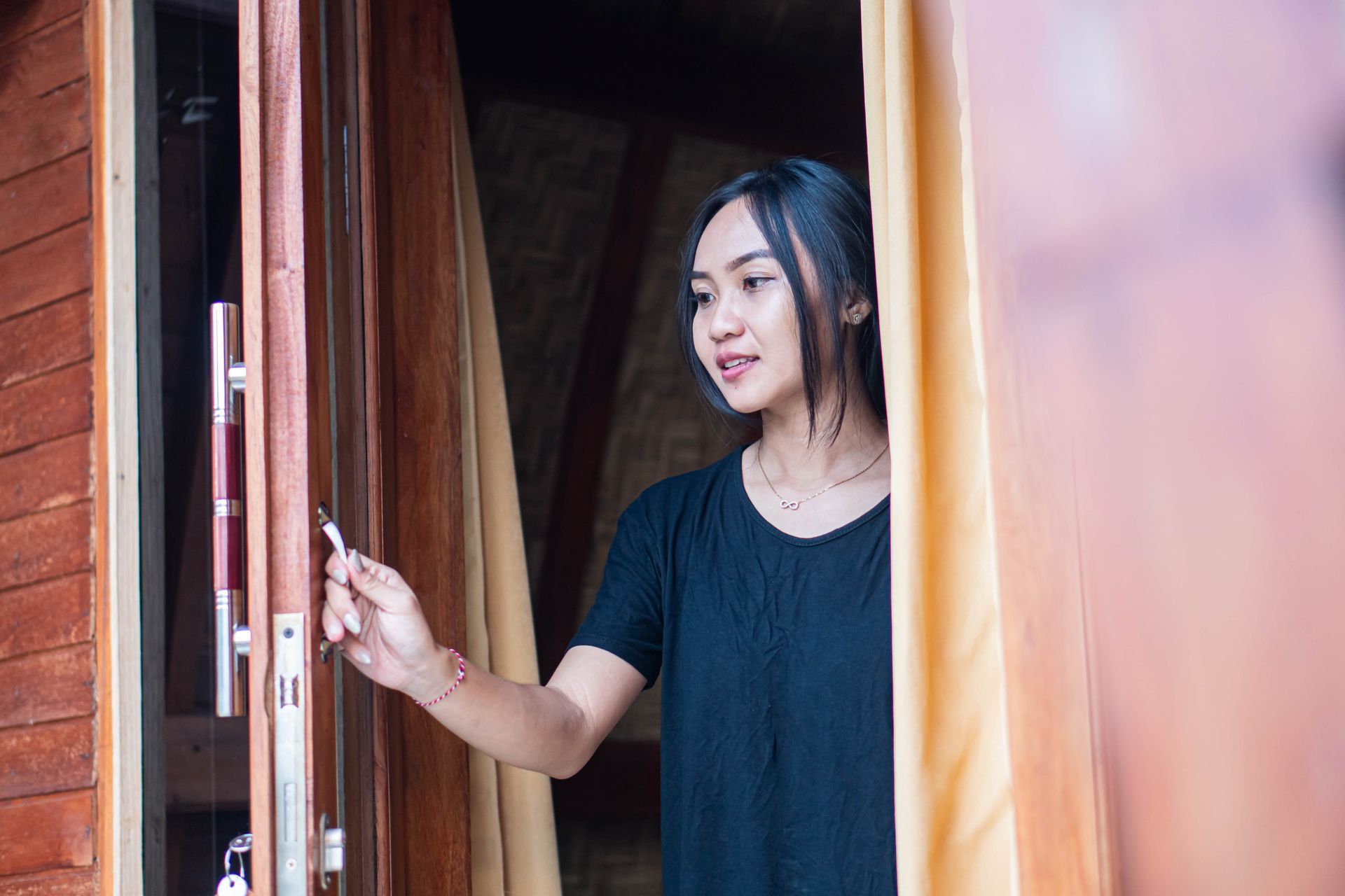 A person in a black t-shirt standing in a doorway and holding a door handle, with gold curtains on the right.