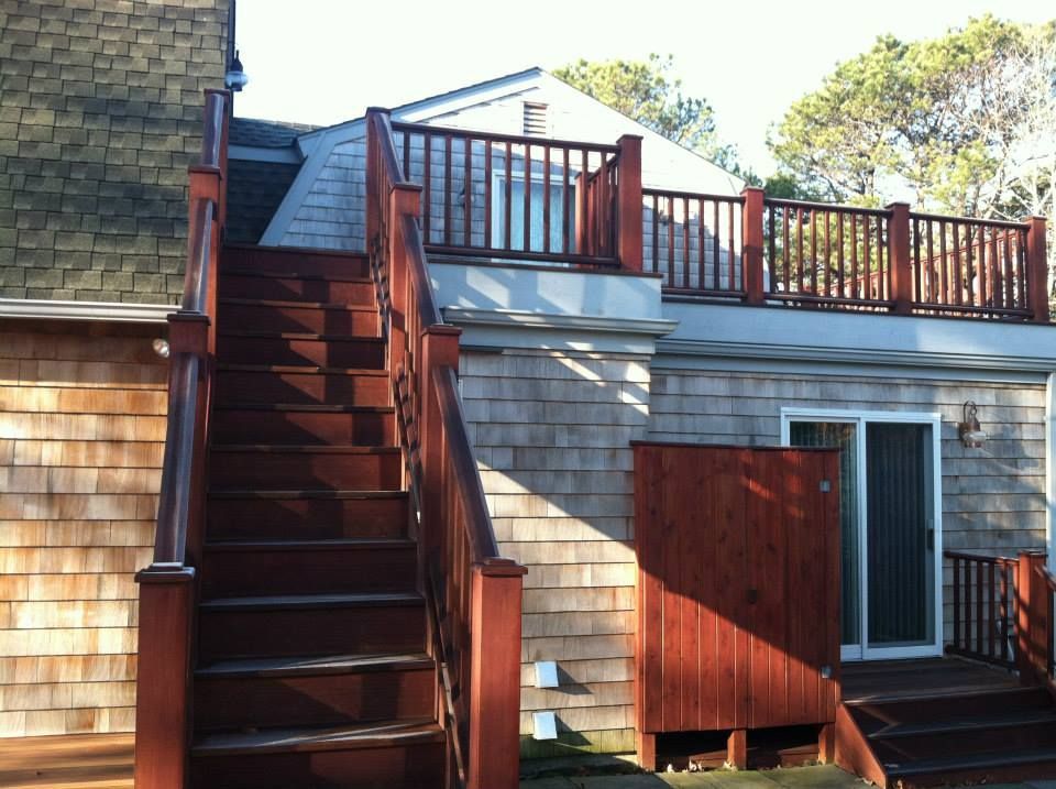 Wooden exterior staircase beside a house deck with red railings and siding