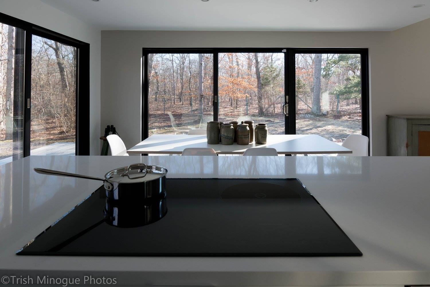 Modern kitchen interior with a white island, stovetop, and large windows overlooking trees