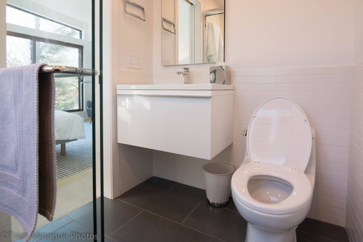 Accessible bathroom with toilet, sink, mirror, and shower curtain beside a glass shower door