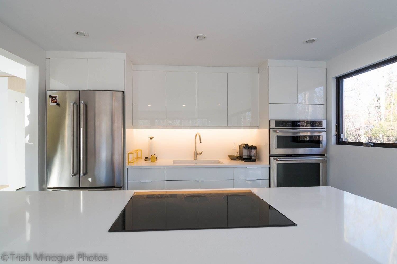 Modern white kitchen with stainless steel appliances and a black induction cooktop on a glossy island.