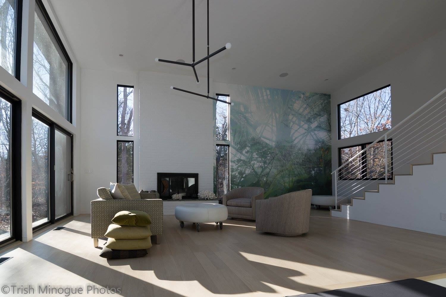 Modern living room with floor-to-ceiling windows, white walls, green chair, round table, and large mural artwork