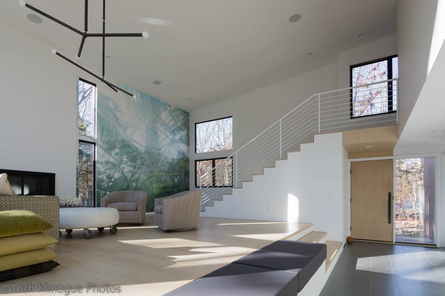 Bright modern living room with white stairs, large windows, and a mural wall.