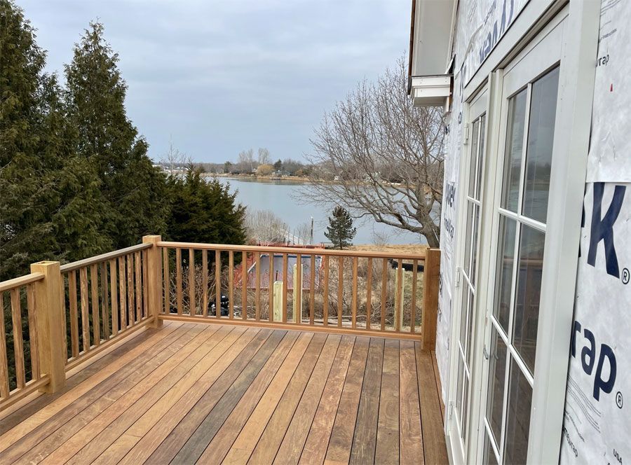 Wooden deck overlooking a lake beside a house, with railing and trees in the background.