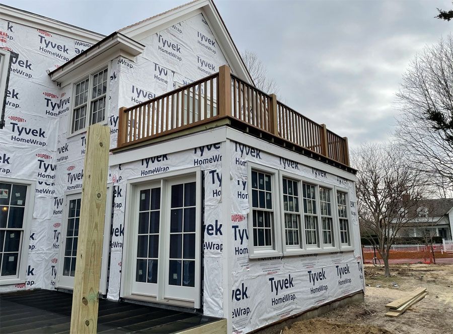 Two-story house under construction with Tyvek wrap and a wooden rooftop deck, viewed from the side.