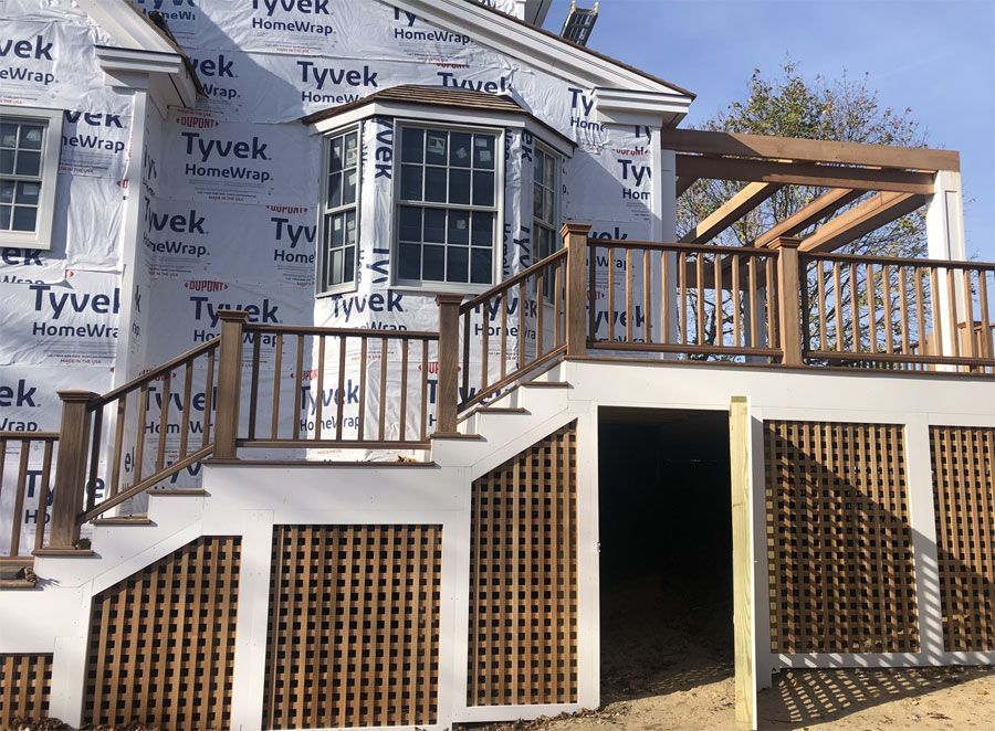 House under construction with Tyvek wrap, white trim, a staircase, and wooden railings on a raised deck