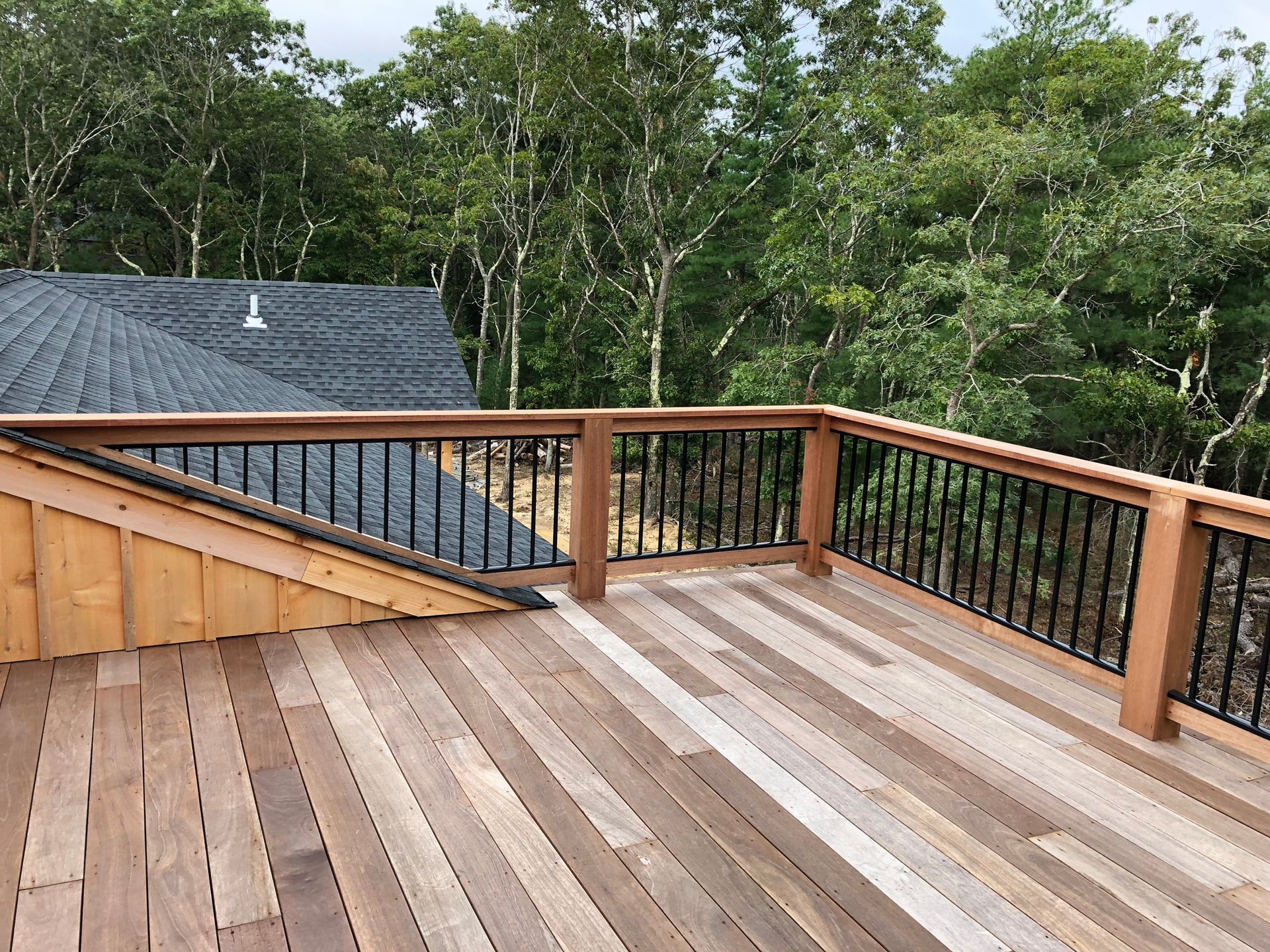 Wooden rooftop deck with railing, overlooking trees and a nearby shingled roof