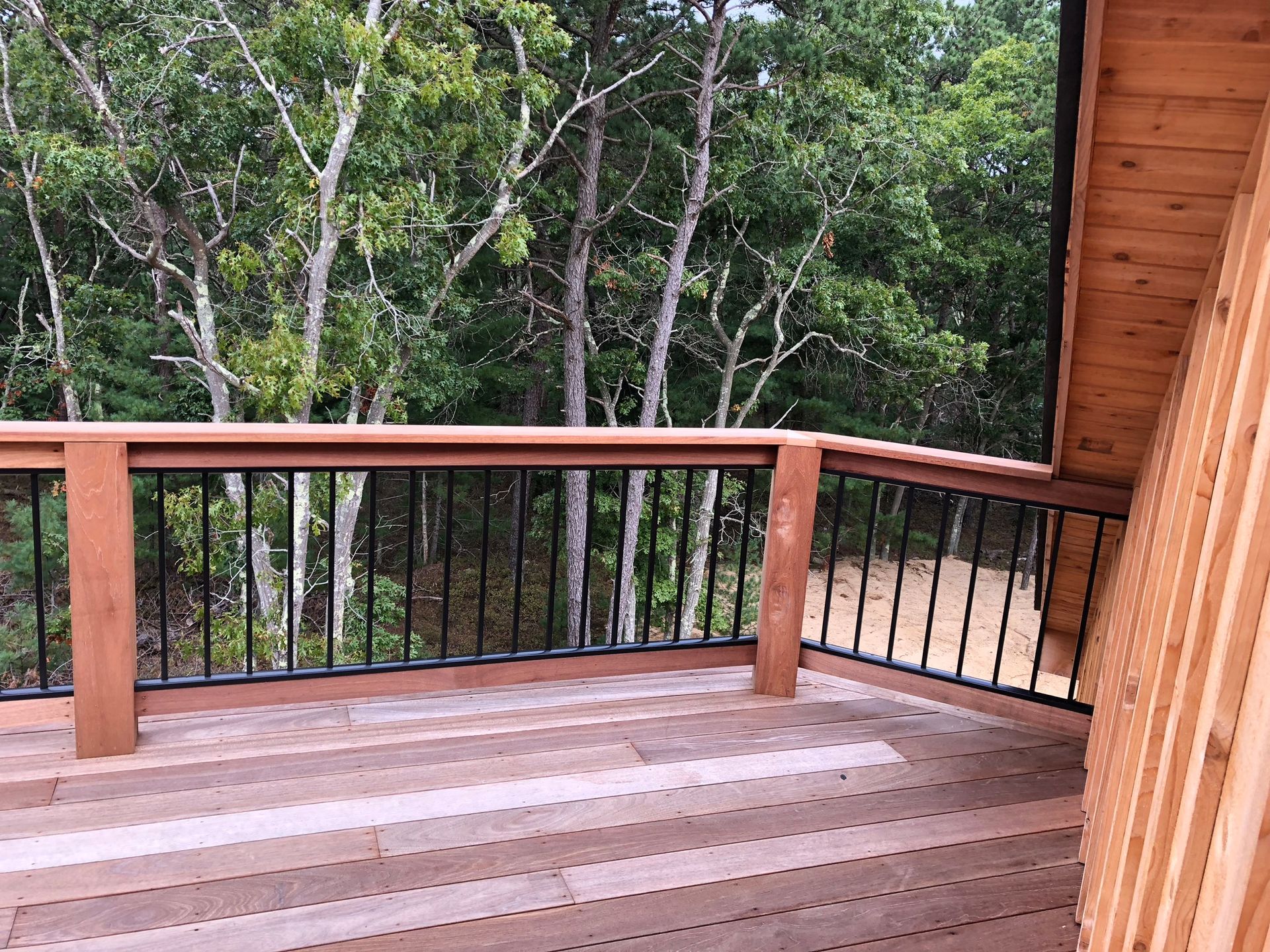 Wooden deck with brown railing overlooking dense green trees and forest.