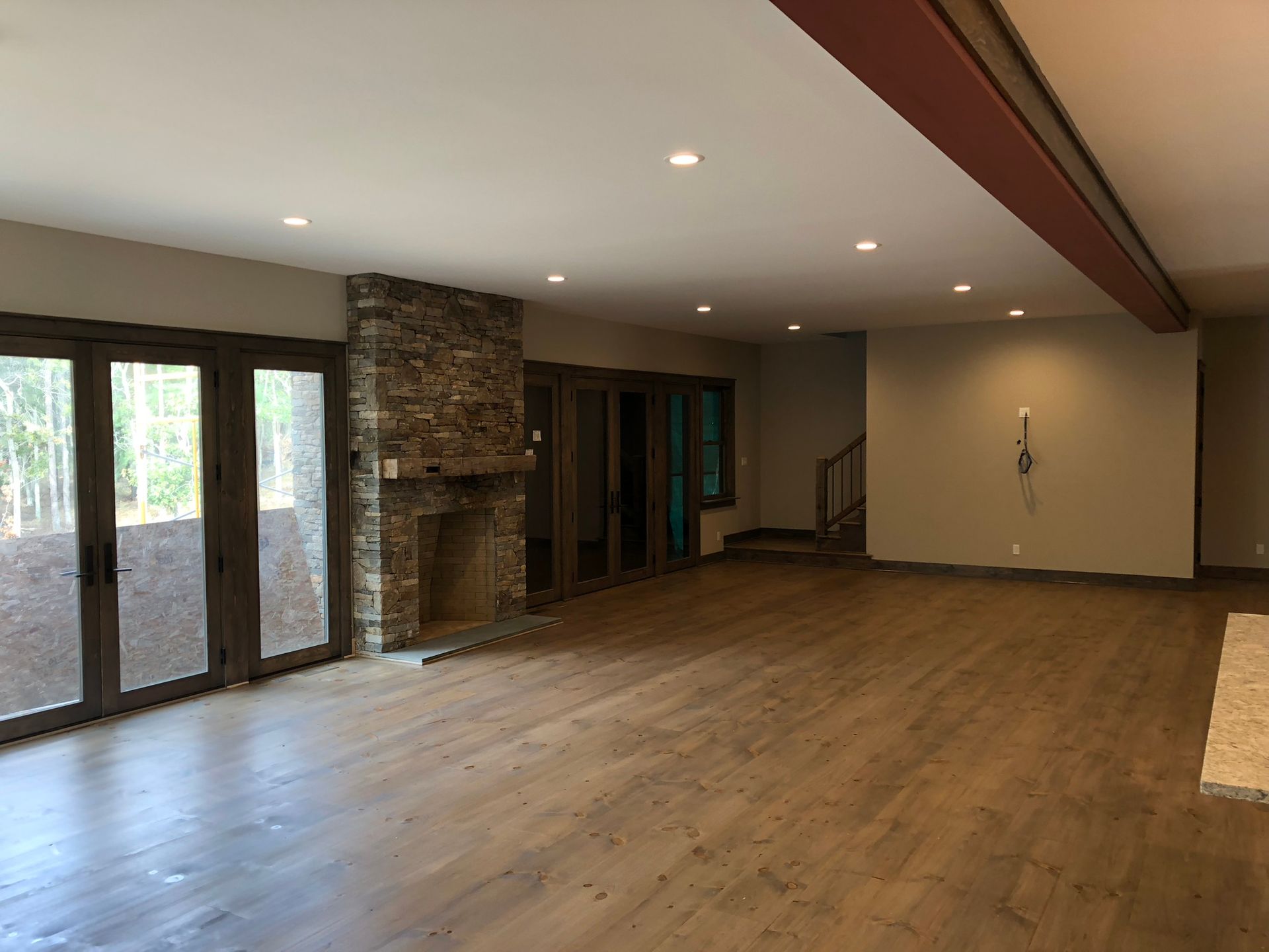 Empty living room with wood floors, stone fireplace, and large glass doors.