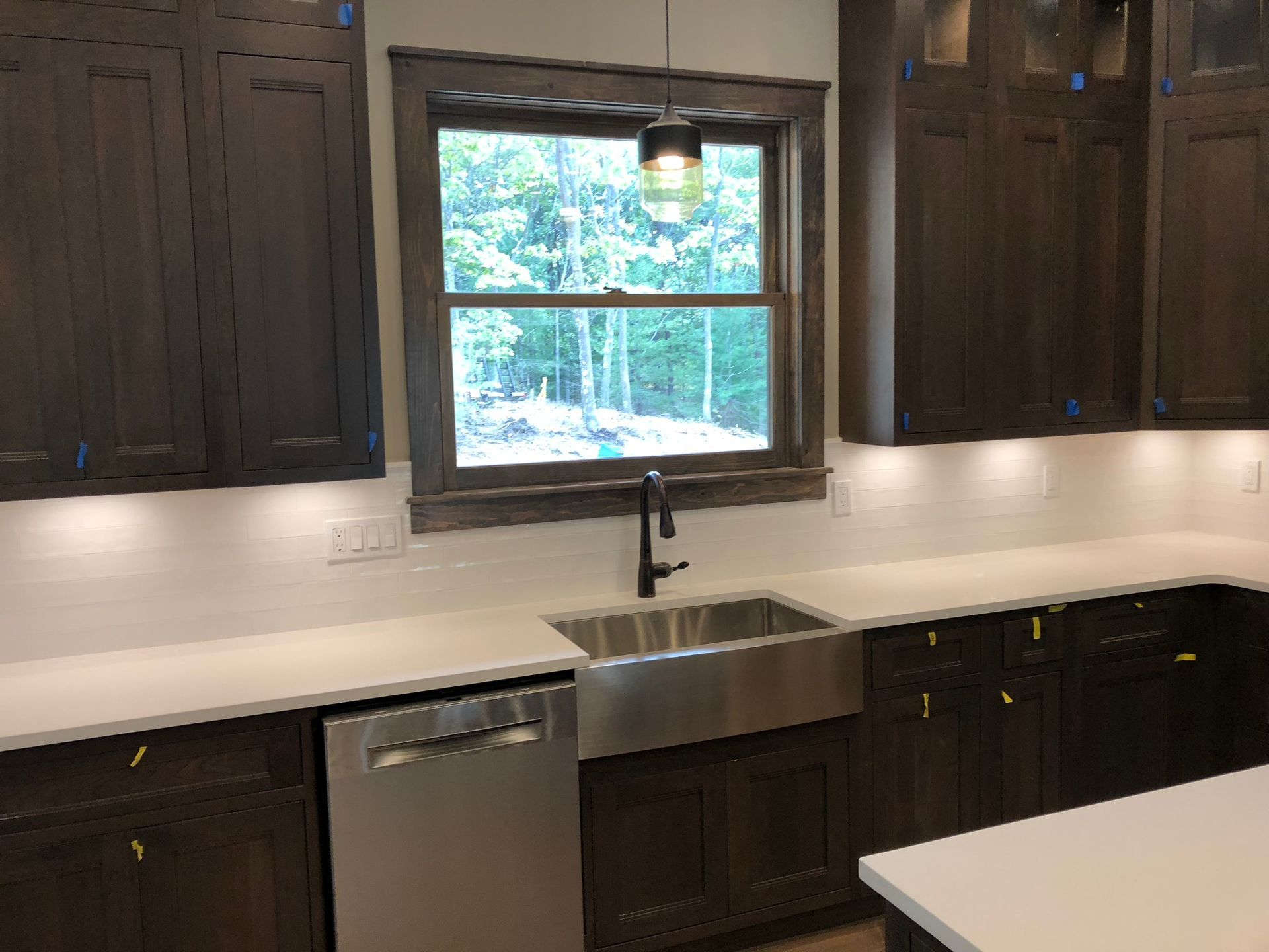 Modern kitchen with dark wood cabinets, white countertops, a farmhouse sink, and a window above the sink.