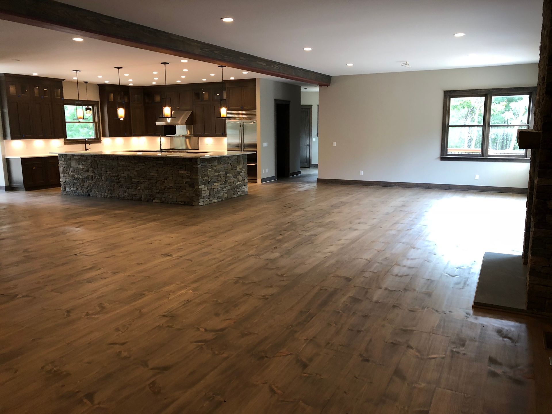Empty open-plan living area with wood floors, a kitchen island, and large windows.