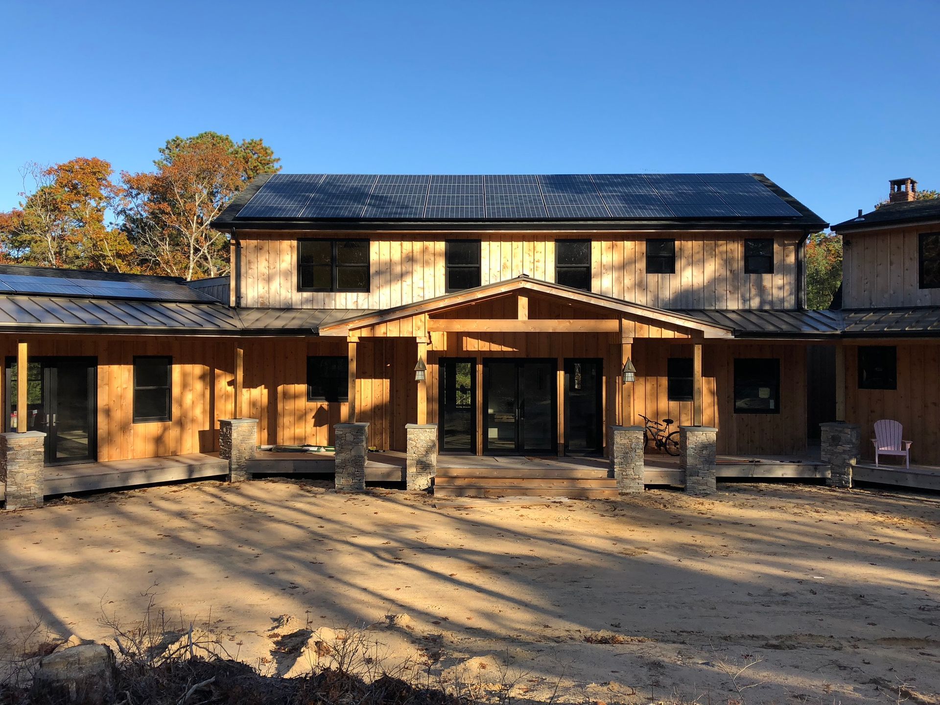 Rustic two-story wooden house with a covered porch and metal roof in a sunny yard