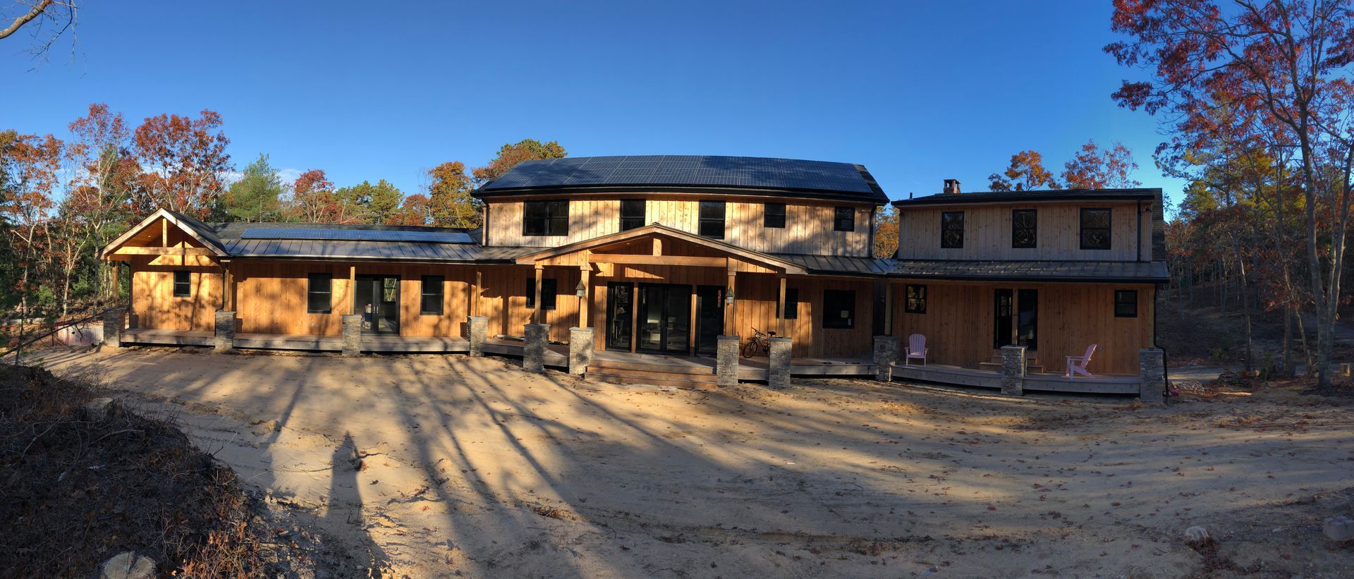 Large unfinished two-story house with wooden framing and brick walls in a wooded lot at sunset