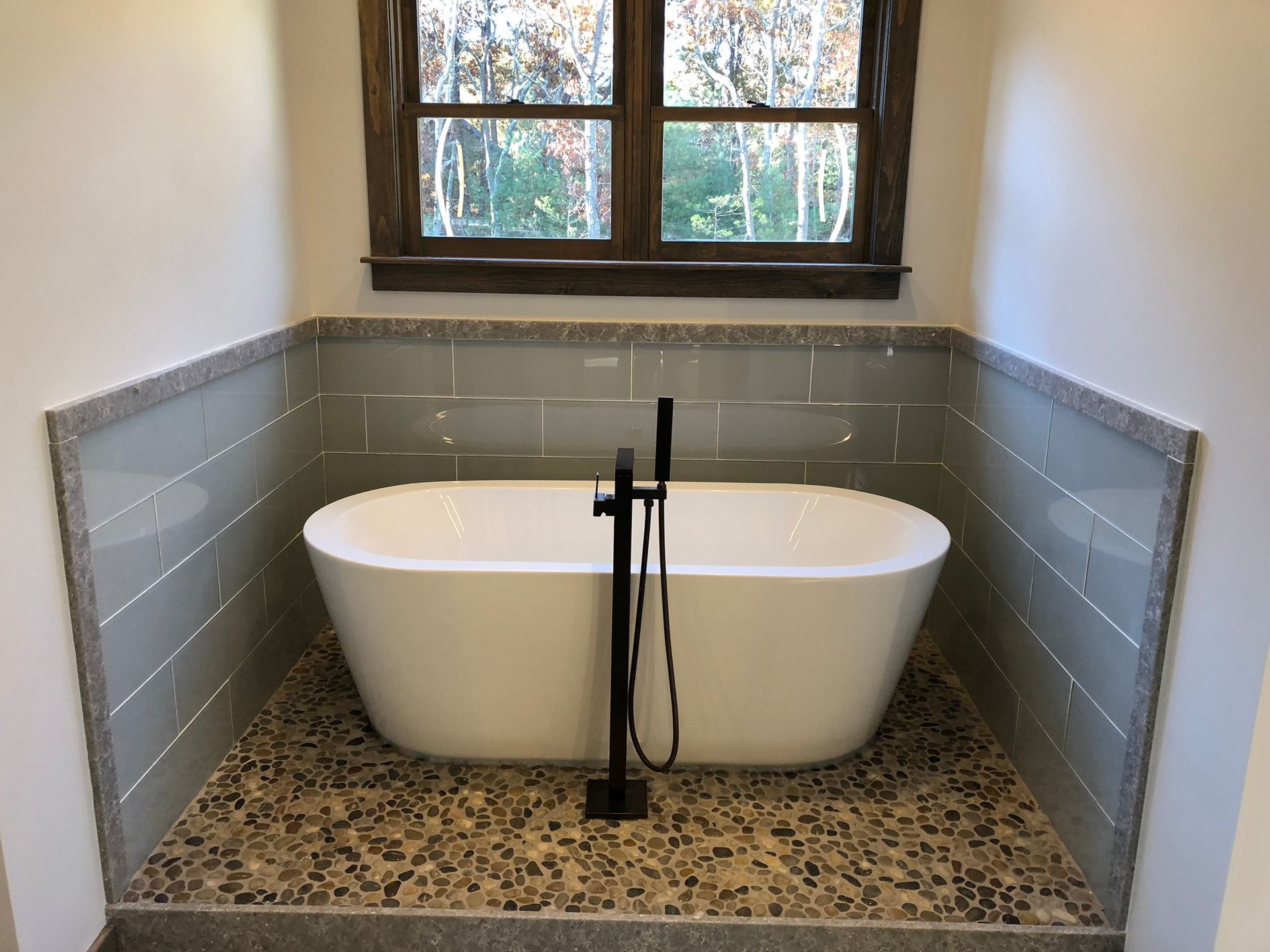 Bathroom with a freestanding tub in a tiled alcove beneath a window.