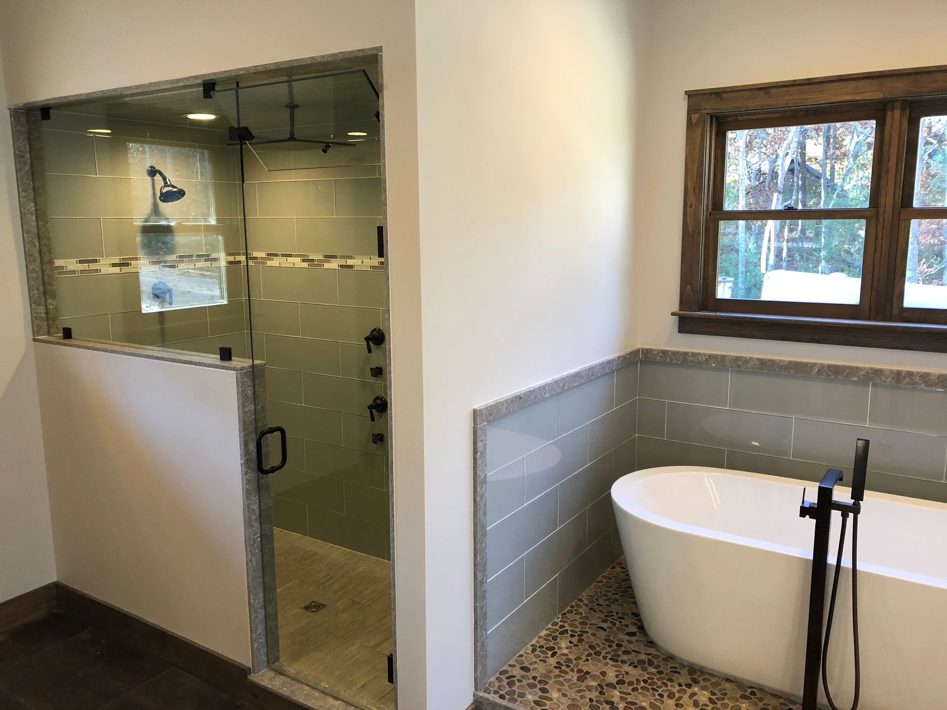 Modern bathroom with glass shower enclosure, freestanding tub, and window above tiled wainscoting
