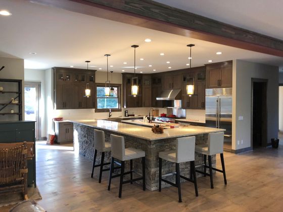 Modern kitchen with large island, bar stools, pendant lights, and wood cabinets in an open floor plan.