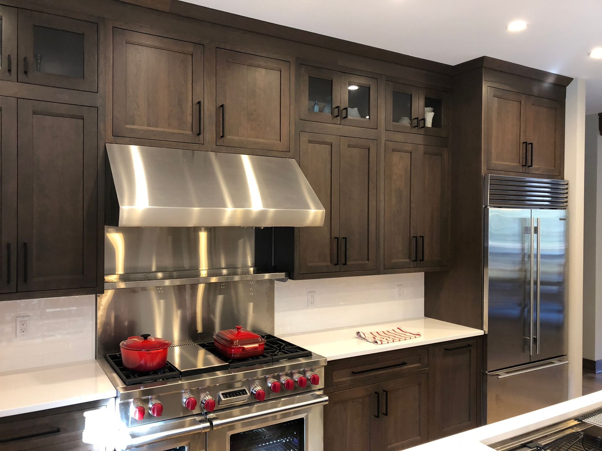 Modern kitchen with dark wood cabinets, stainless steel stove and hood, white countertops, and a large fridge
