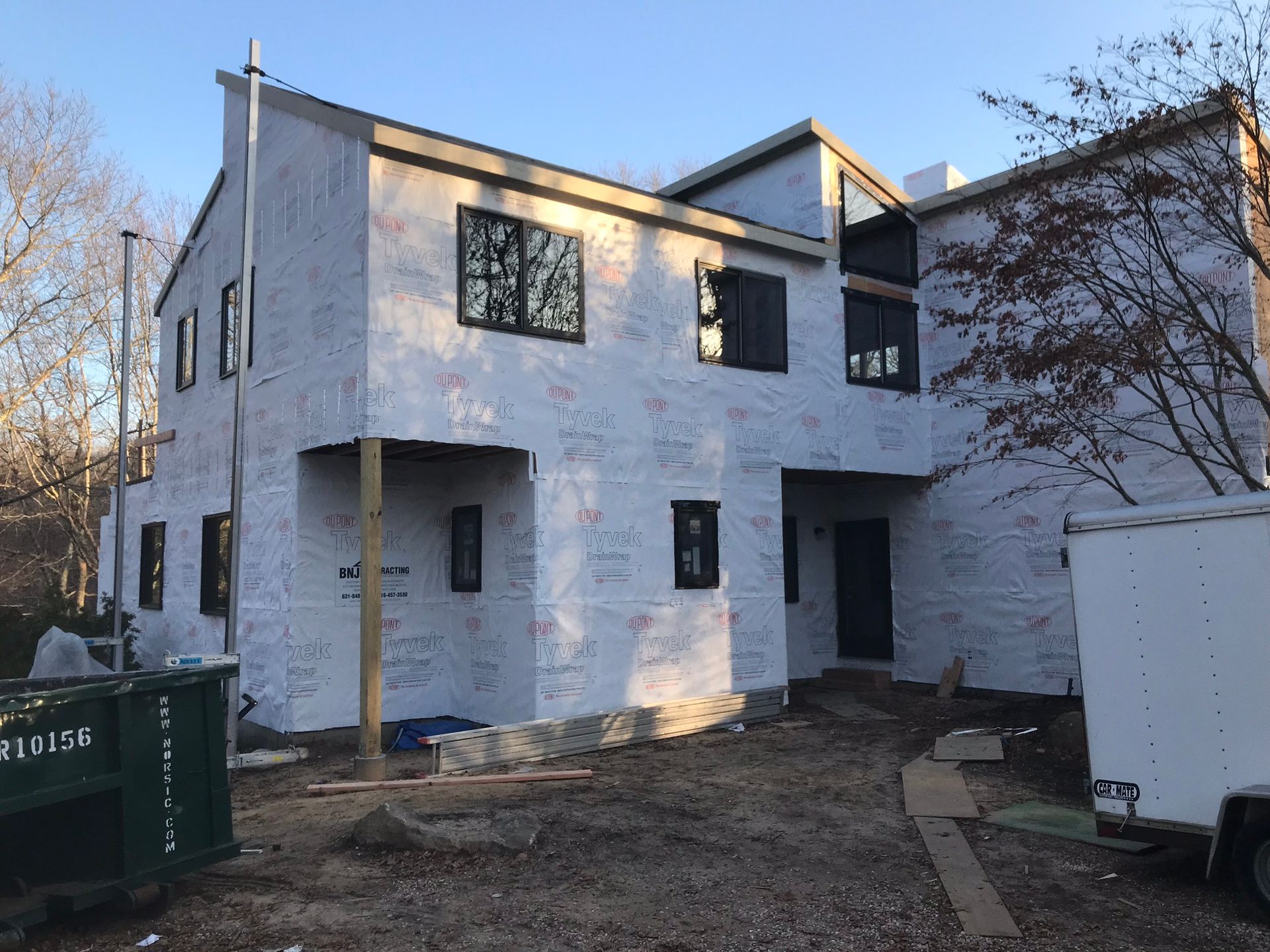 Two-story white house under construction with dark window frames and a bare yard at dusk