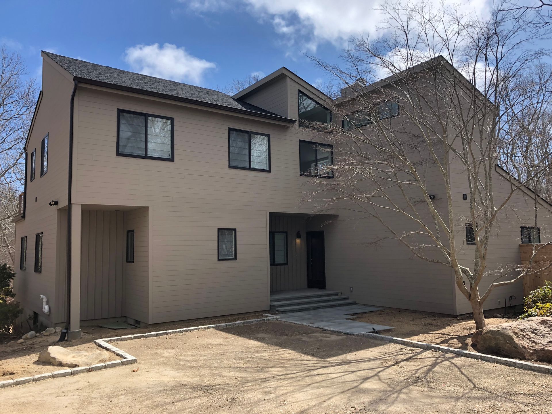 Two-story beige house with a covered entry and leafless tree in front under a blue sky