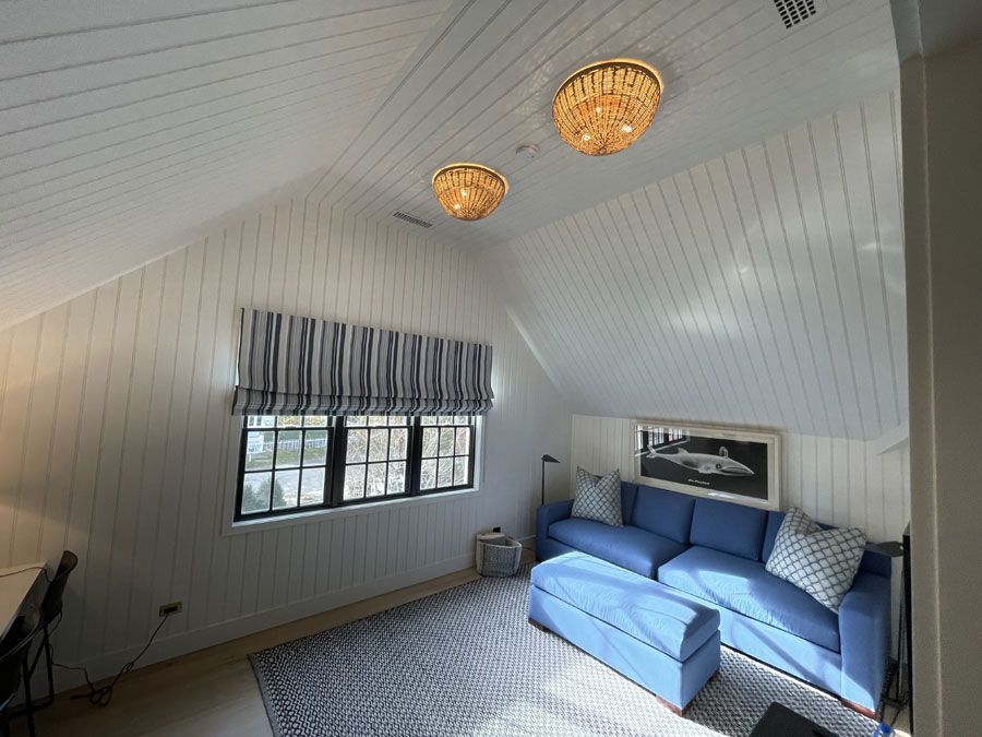 Bright attic living room with blue sofa, striped window blind, and woven ceiling lights
