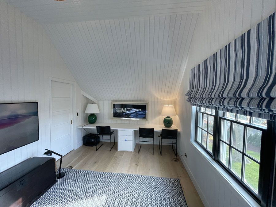 Bright home office with white walls, black desk, striped window shade, and a wall-mounted TV