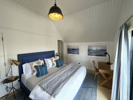 Bright bedroom with blue bed, striped runner, desk, framed wall art, and skylight ceiling