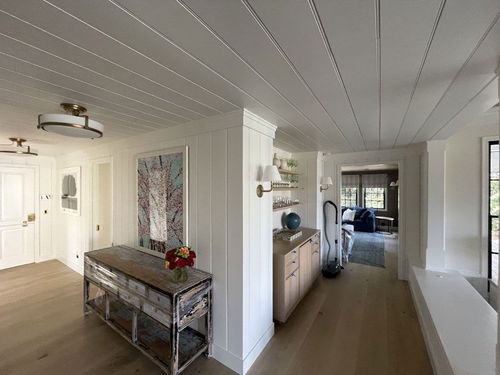 Bright, airy hallway with white walls, wood floors, a console table, and a view into a living room.