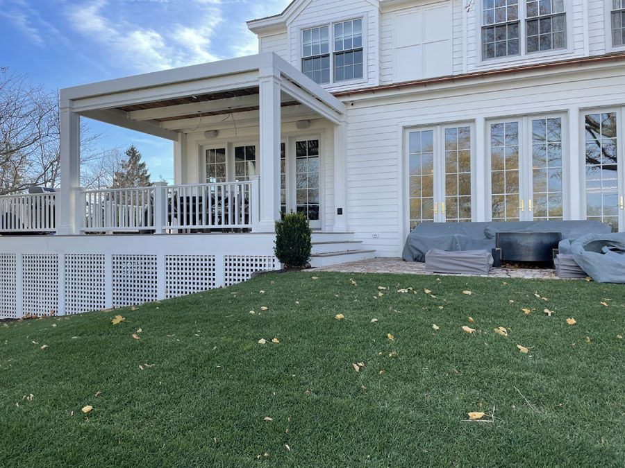 White house with a porch, lawn, and patio seating under a partly cloudy sky