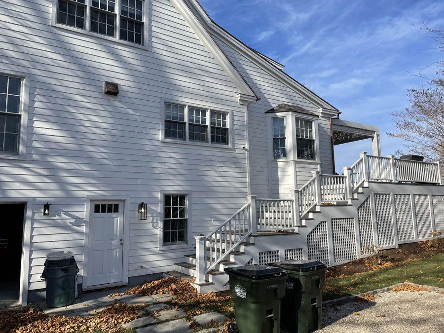 White house exterior with stairs, porch railing, windows, and trash bins in the yard