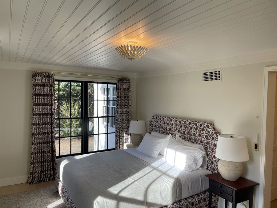 Bright bedroom with a bed, bedside lamps, French doors, and sunlight streaming across the floor