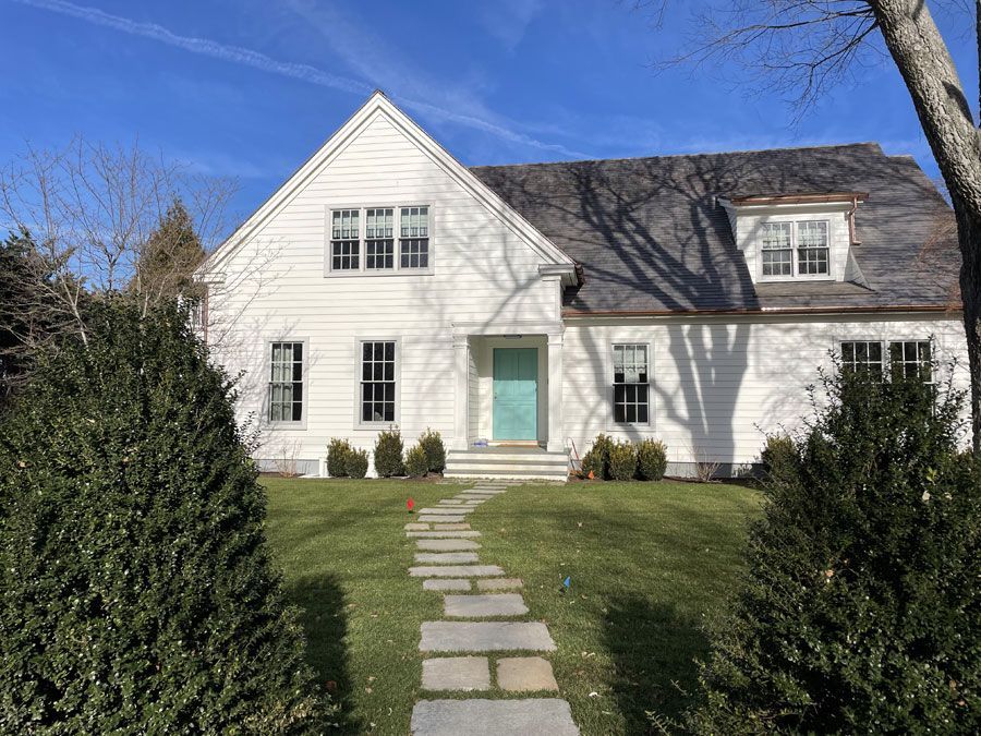White house with teal front door and stone path leading through a green lawn.