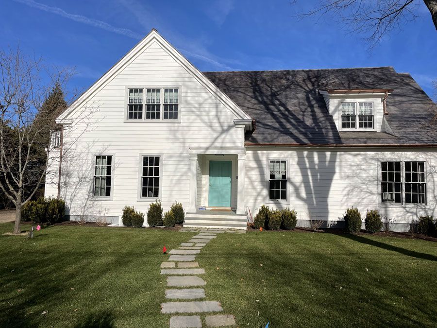 White house with a teal front door, stone path, and green lawn under a blue sky