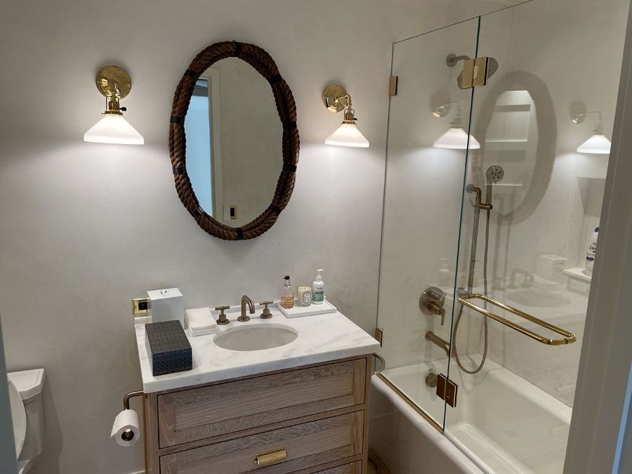 Compact bathroom with vanity, oval mirror, wall sconces, and glass shower/tub.