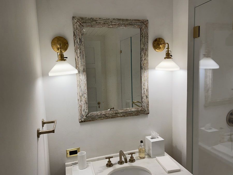 Bathroom vanity with ornate mirror, brass sconces, and white sink against a light wall.