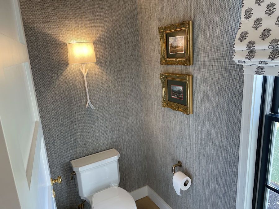 Small bathroom with gray textured walls, toilet, wall sconce, and framed art.
