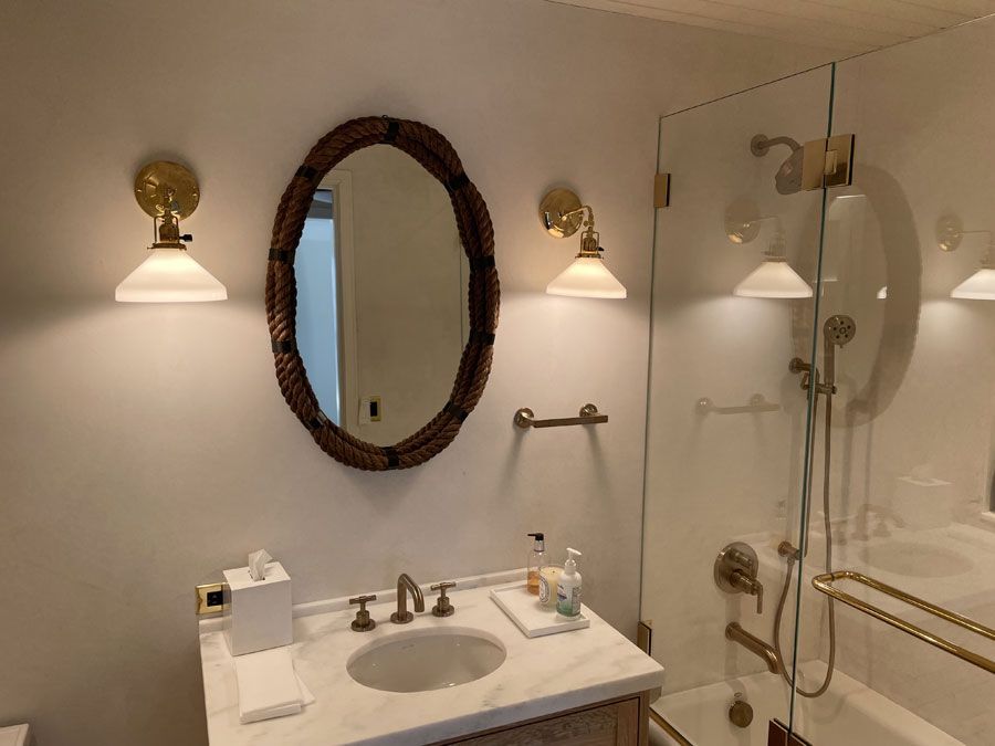Bathroom vanity with oval mirror, wall sconces, and glass shower door.