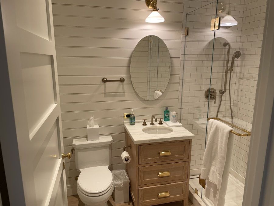 Small white bathroom with toilet, vanity, oval mirror, and shower/tub with towel rack