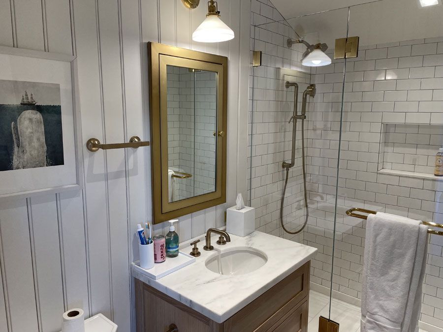 Modern bathroom with white tile, gold fixtures, vanity, shower, and hanging towels