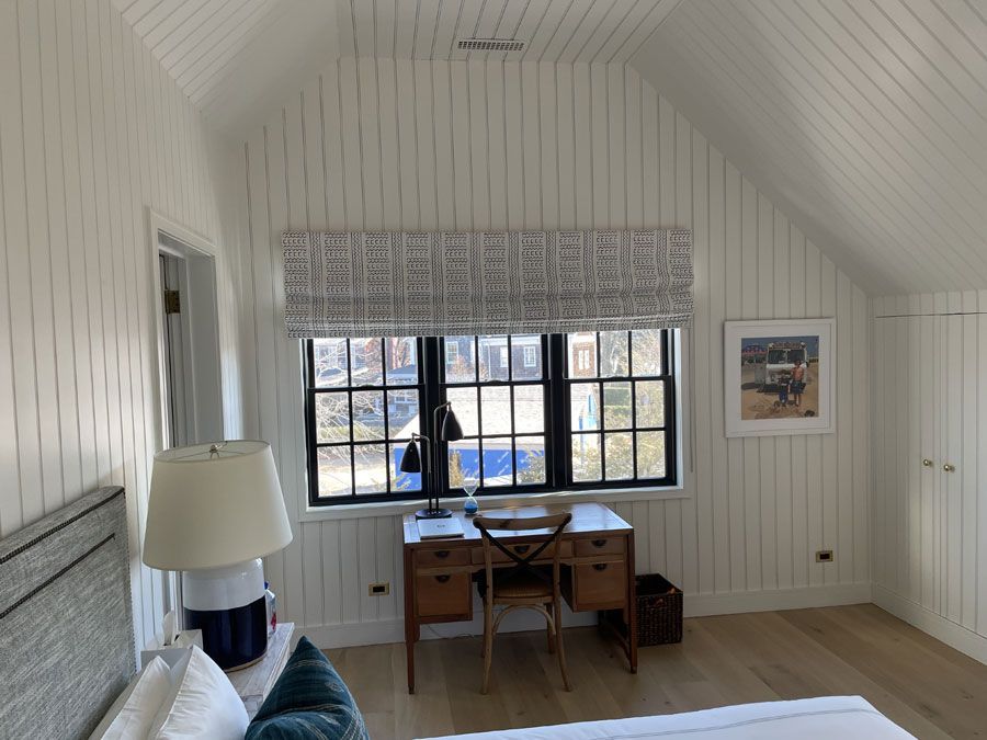 Bright attic room with a desk, chair, window, lamp, and white paneled walls.