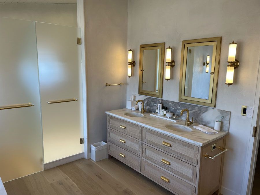 Modern bathroom with double vanity, mirrors, and frosted glass shower doors in neutral tones