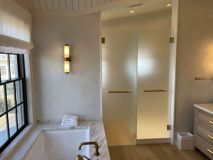 Bright bathroom with freestanding tub, frosted glass shower doors, vanity, and large window.