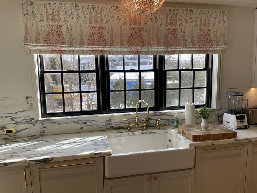 Bright kitchen sink beneath a black-framed window with floral valance and countertop items nearby